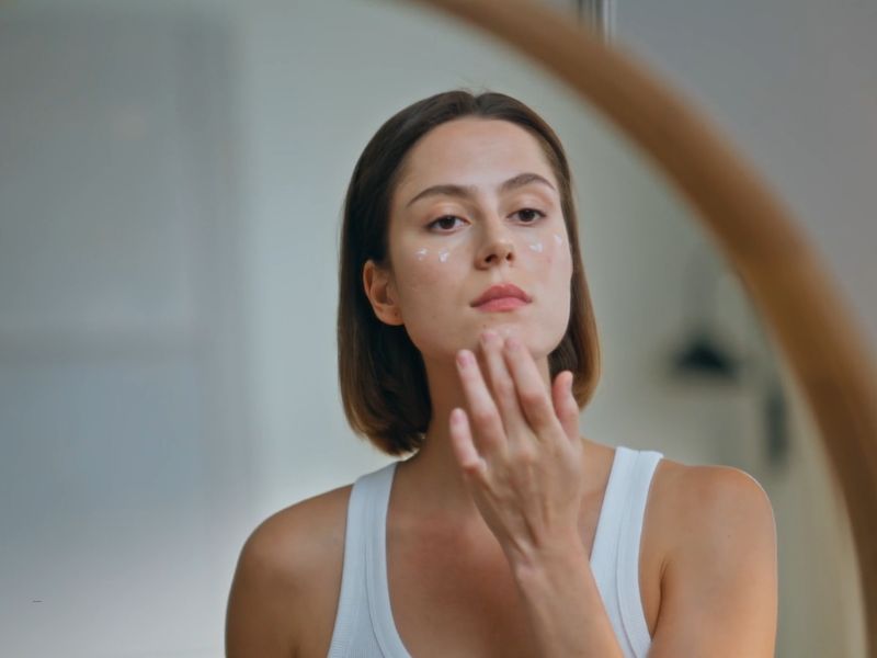 devojka nanosi kremu na lice